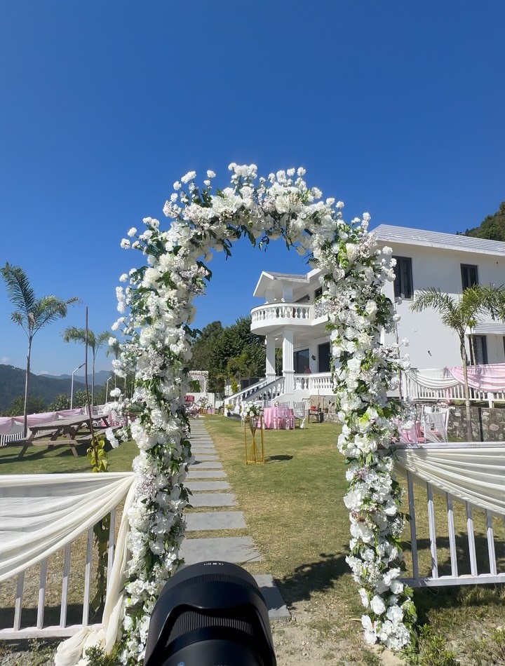 A white floral arch framing a celebration venue beneath a clear blue sky in Bhimtal